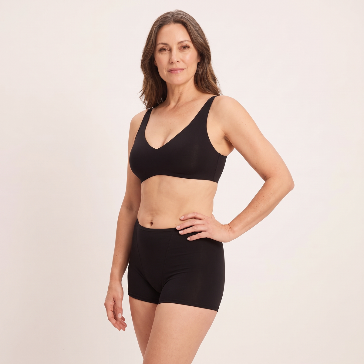 A woman modeling a black bralette and matching high-waisted compression shorts against a plain light beige studio background.