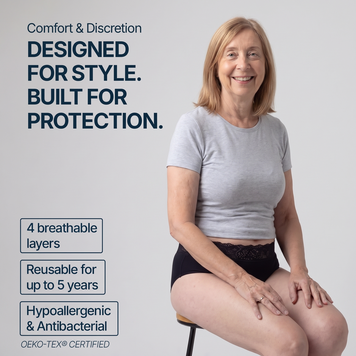 A woman seated on a stool wearing a light gray reusable protective shirt and black underwear, with marketing text on a light gray background. The text highlights comfort, discretion, breathable layers, reusability for up to 5 years, hypoallergenic and antibacterial properties, and OEKO-TEX certification.