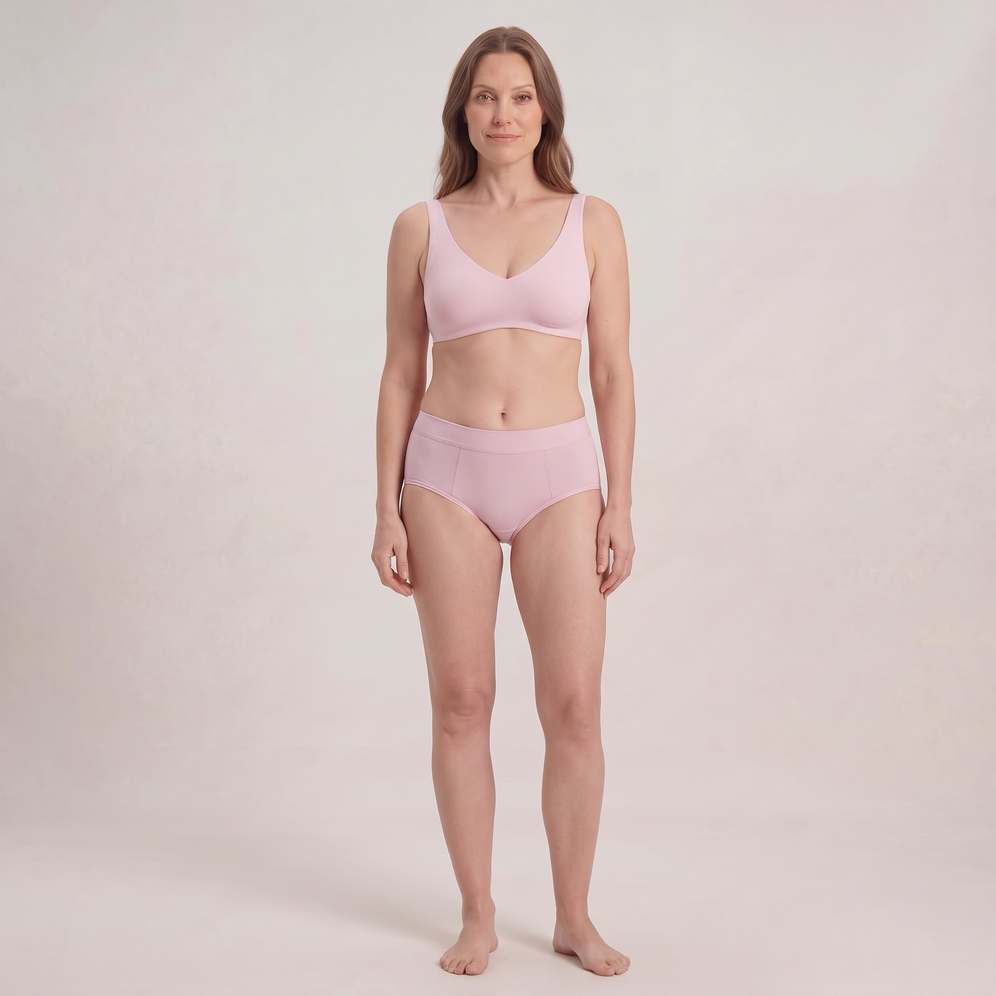 A woman stands facing forward in a studio wearing a light pink bra and matching high-waisted briefs.